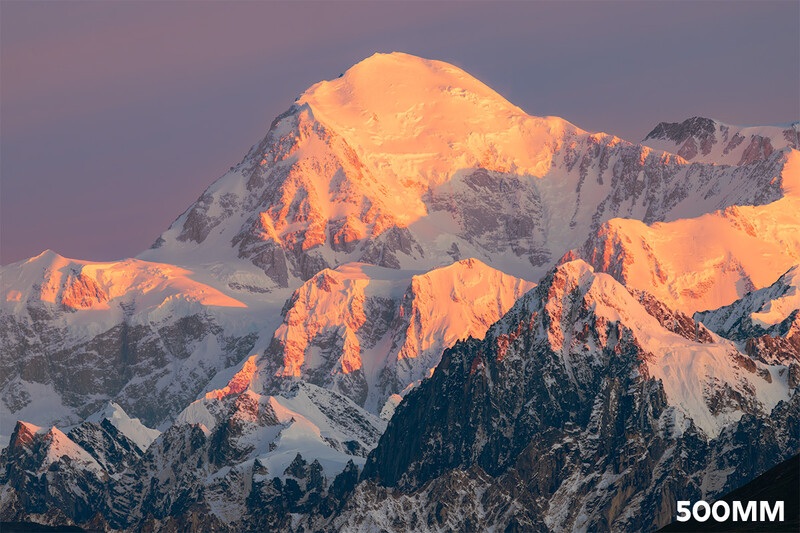 Snow-covered mountain peaks illuminated by golden sunrise light against a purple-blue sky.