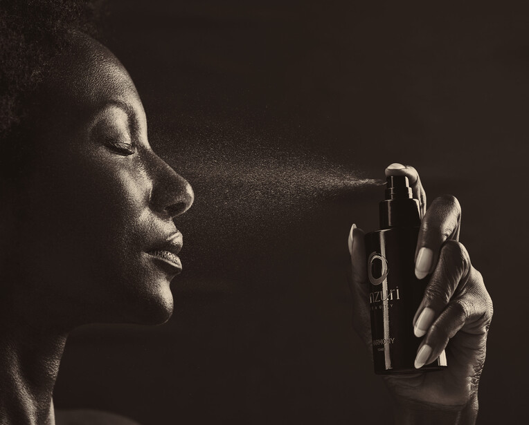 Woman spraying perfume or fragrance from a bottle against a dark background.