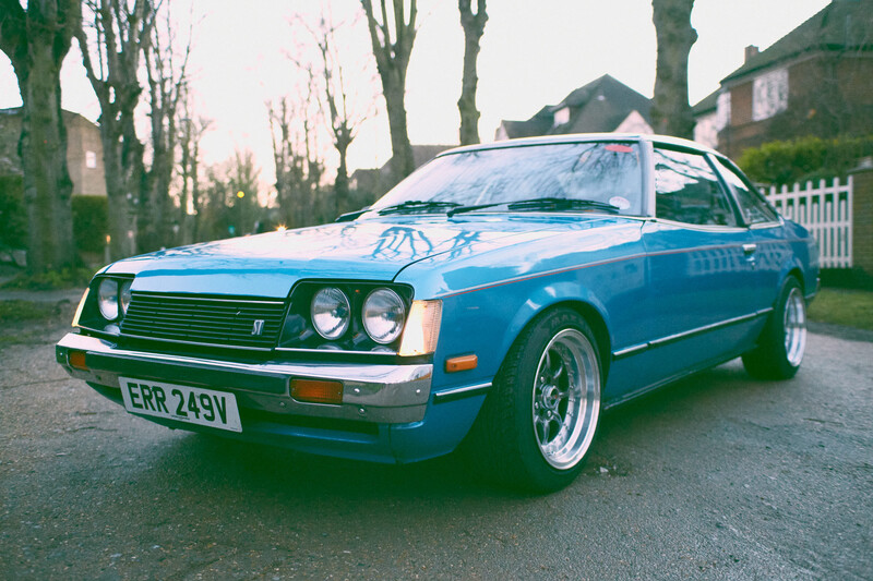 Bright blue coupe parked on a residential driveway lined with bare trees.