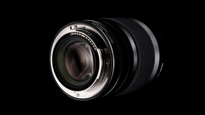 Prime camera lens with fast aperture and chrome bayonet mount against black background.