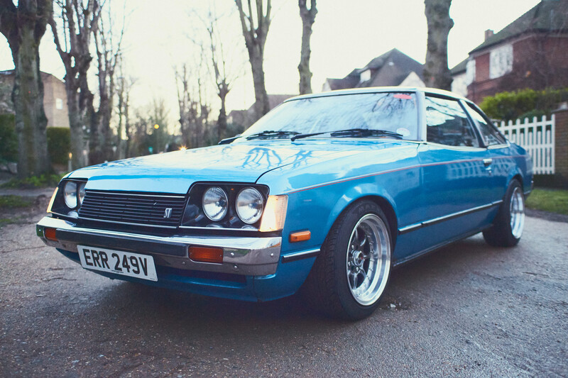 Bright blue coupe parked on a residential driveway lined with bare trees.