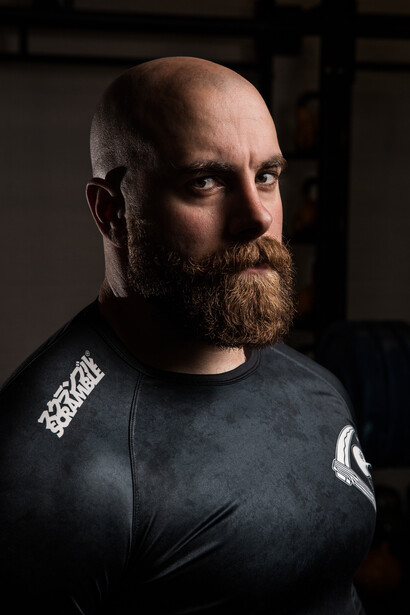 Bearded man with bald head wearing dark graphic t-shirt against neutral background.