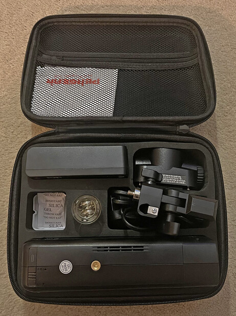 Open hard case containing camera gimbal, batteries, charging cables, and memory cards.