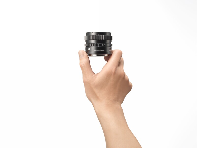 Hand holding a compact camera lens against a white background.