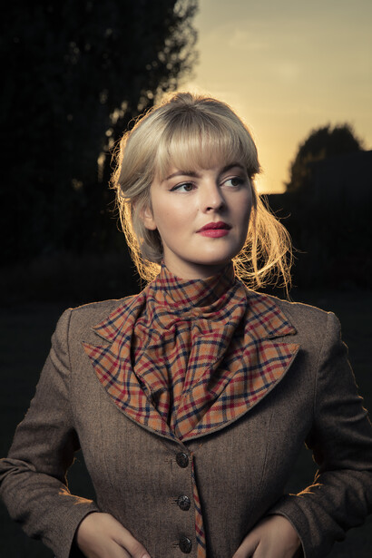 Woman in plaid blazer and collared shirt photographed outdoors at golden hour.