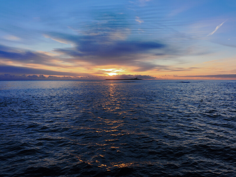 Seascape at sunset with calm ocean, golden sunlight reflecting off water, and colorful sky with blue and pink clouds.