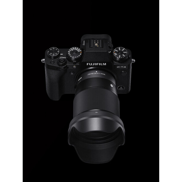 Fujifilm mirrorless camera with telephoto lens mounted, shot from above against black background.
