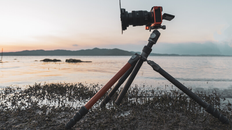 Camera mounted on tripod shooting at sunset over coastal waters with mountains in the distance.