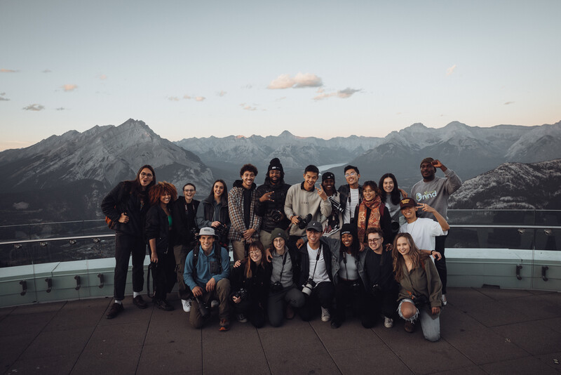Large group of people posing together on an elevated outdoor platform with mountains in background at dusk.