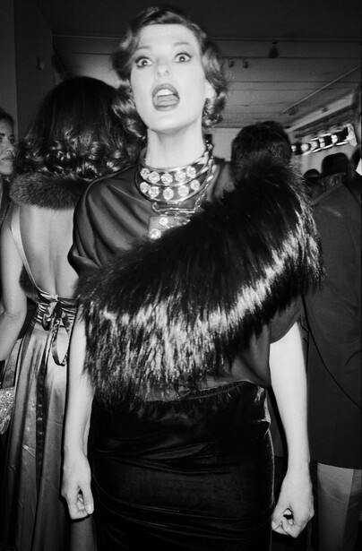 Woman in black evening wear with fur stole and statement necklace at formal event.