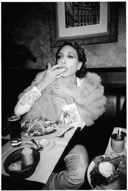 Woman at dining table smoking cigarette while eating, captured in black and white portrait.