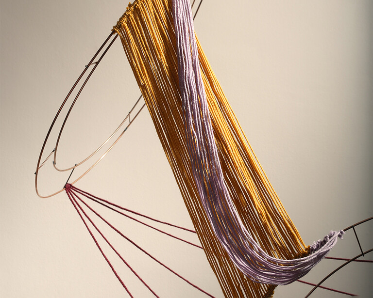 Close-up of strands of hair in gold, purple, and brown tones arranged in a fan pattern against a neutral background.