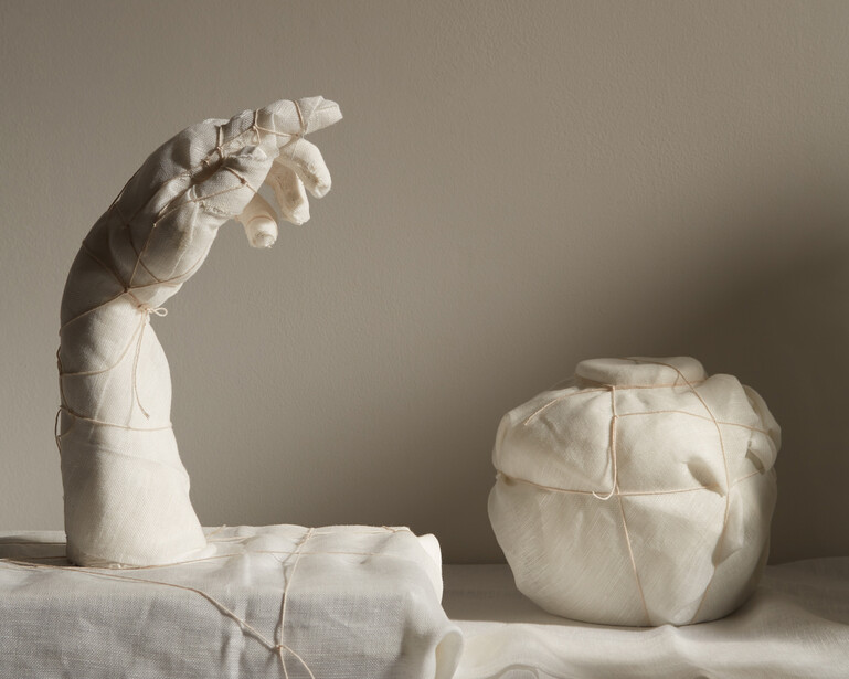 Two white plaster cast sculptures on draped fabric against a neutral background.