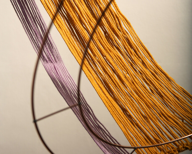 Close-up of purple and golden-yellow strands of thin fiber or thread against a light background.