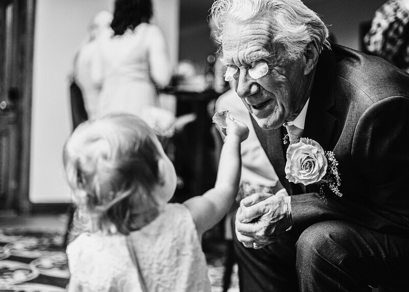 Elderly man in formal attire leaning down to interact with a young child at what appears to be a social gathering.