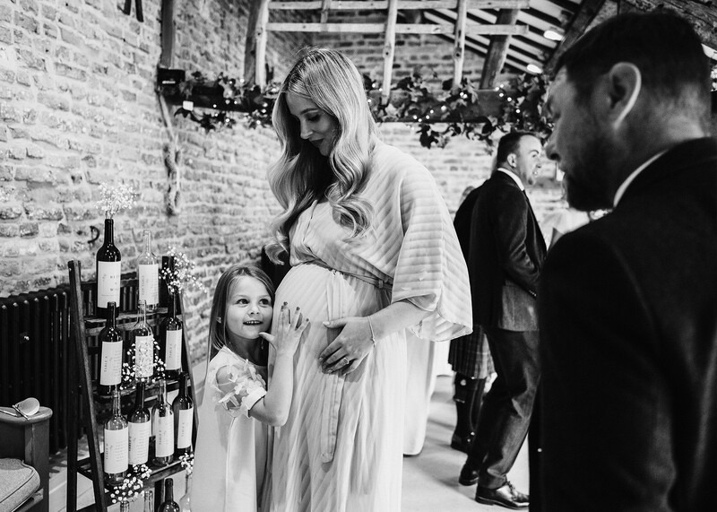 Black and white photograph of a pregnant woman in a white dress posing with a young child during an indoor maternity portrait session.