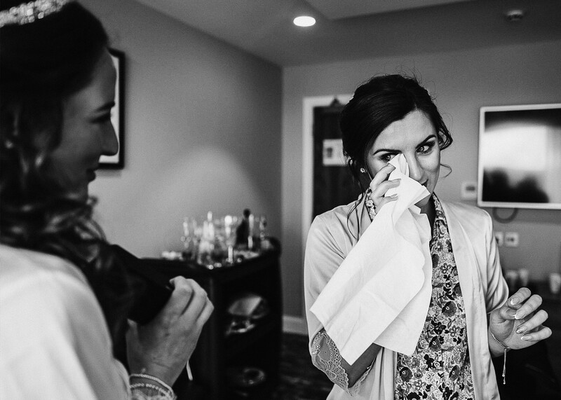 Woman wipes her face with a tissue while conversing with another person in an indoor setting.
