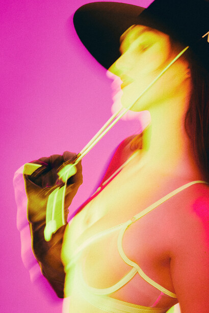 Portrait of a person in a black hat smoking a cigarette against a vibrant magenta background.