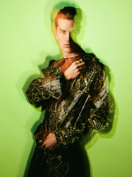 Man in gold patterned jacket against bright green background with soft edge vignette.