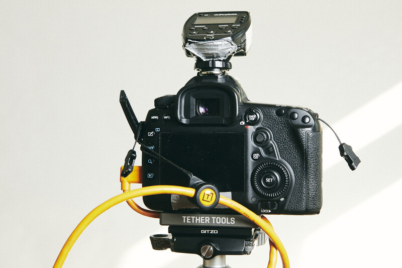 Professional DSLR camera mounted on a rig with yellow tether cable and black mounting hardware against a white background.