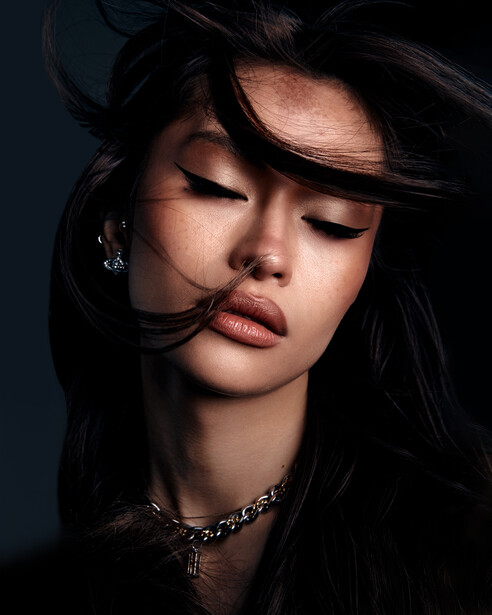 Woman with long black hair and closed eyes against dark blue background, lit with dramatic side lighting.