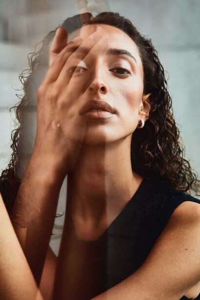 Woman with long dark hair gazing downward, hand near face in contemplative pose.