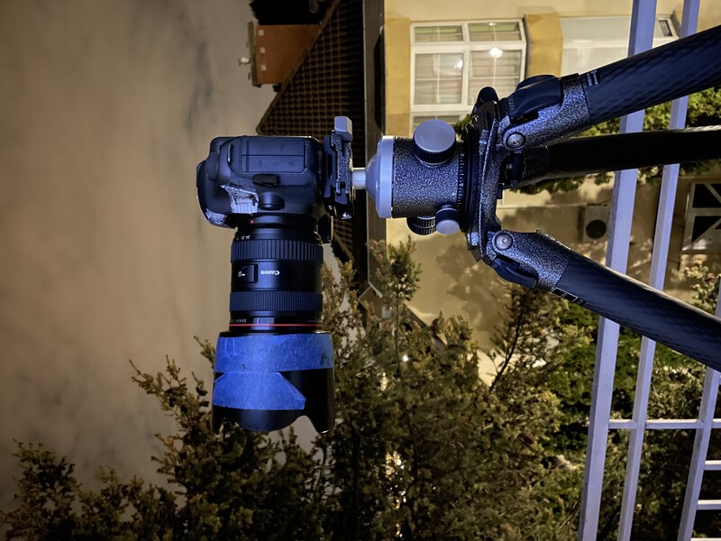Camera and telephoto lens mounted on tripod at night, illuminated by blue LED ring light.