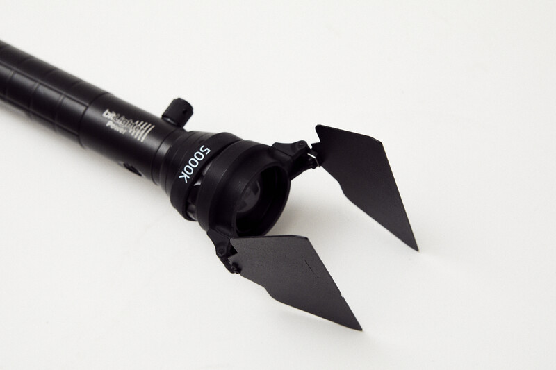 Black barn door light modifier with adjustable flaps mounted on studio lighting rod.