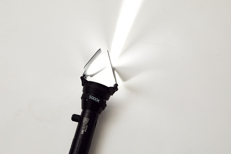 Black flashlight with reflector attachment directing a bright beam of light against a white background.