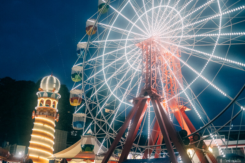 Illuminated Ferris wheel at night with glowing spoked structure and lit carousel tower in foreground.
