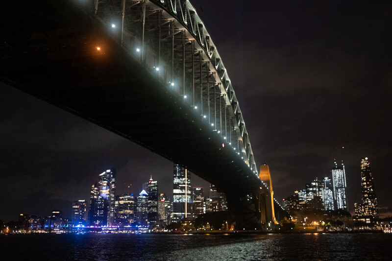Illuminated bridge spanning a waterway at night, with a city skyline glowing in the background.