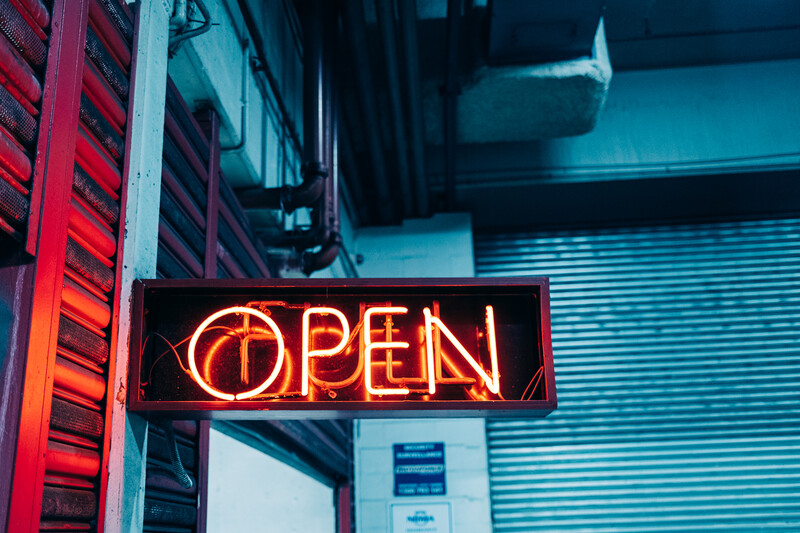 Neon OPEN sign glowing red-orange against dark storefront with corrugated metal shutter.