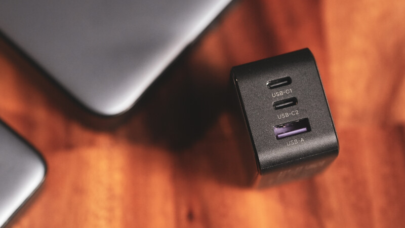Black multi-port USB charging hub with USB-C and USB-A ports displayed on orange and gray background.
