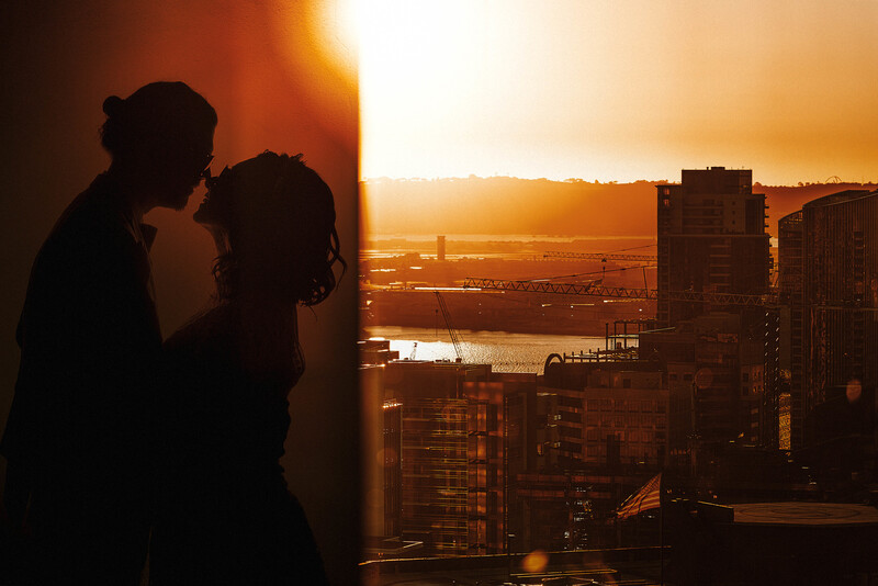 Silhouetted couple embracing on a high-rise balcony during golden hour sunset over a cityscape.