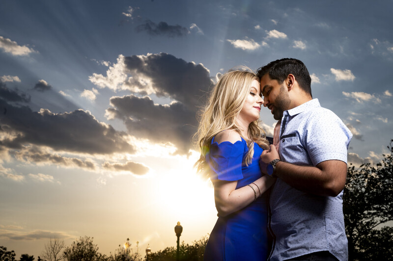 Couple embracing outdoors at sunset with dramatic cloudy sky and golden light behind them.