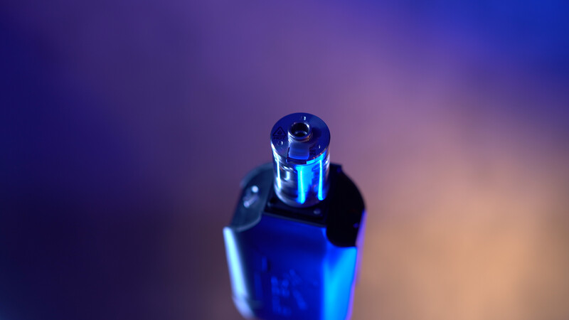 Blue perfume bottle with spherical cap against blurred purple and warm-toned background.