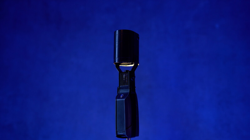 Studio flash with modeling light mounted on stand against deep blue background.