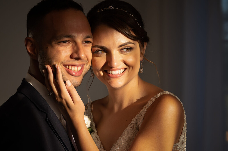 Smiling couple in formal attire posing closely together with warm side lighting.