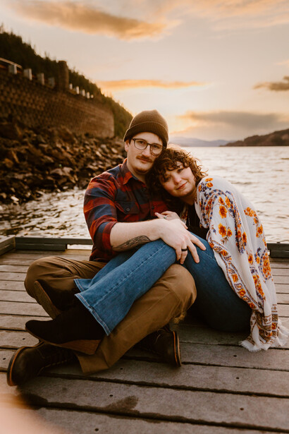Couple sitting together on a wooden dock by the water during golden hour.