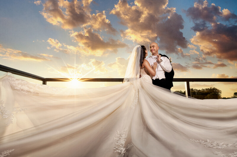 Bride and groom embracing on a rooftop at sunset, with flowing veil billowing in the wind.