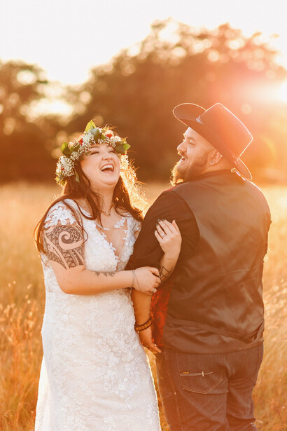 Couple in western attire posing together during golden hour in an open field.
