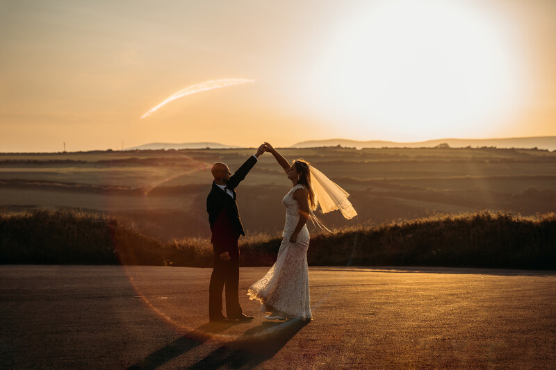 Bride and groom forming a heart shape with their arms during golden hour sunset.
