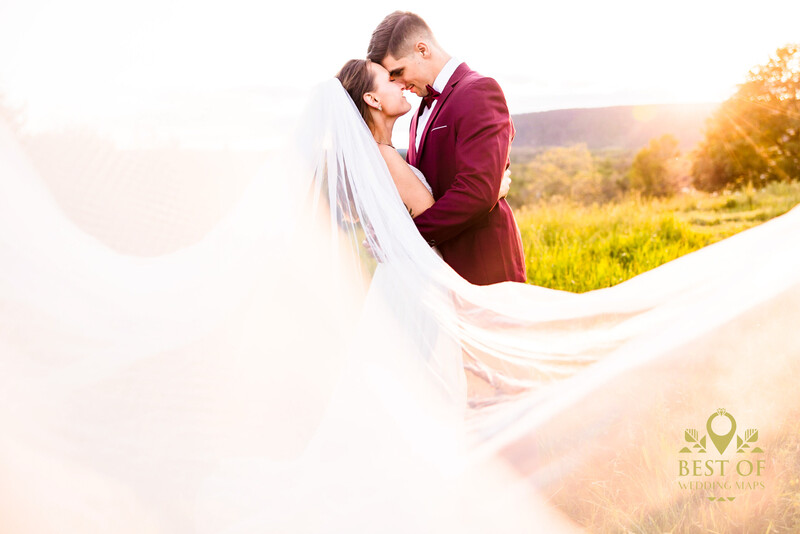 Bride and groom kissing outdoors during golden hour with flowing veil.