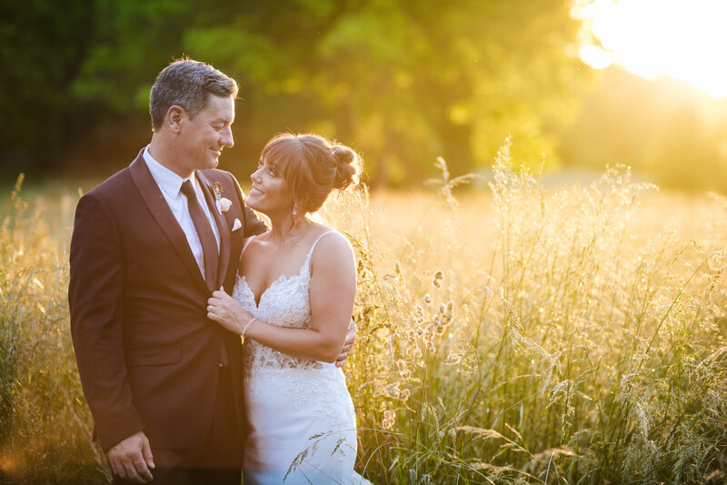Bride and groom standing in a sunlit field during golden hour.