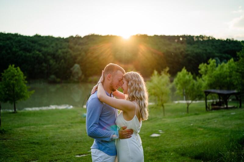 Couple embracing during golden hour with forested landscape and water in background.