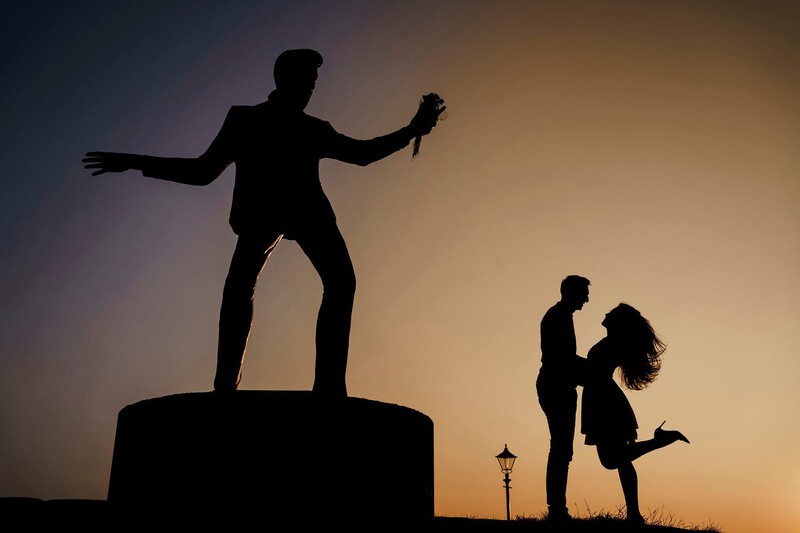 Silhouettes of three people against a golden sunset sky, with one figure standing on an elevated platform with arms outstretched.