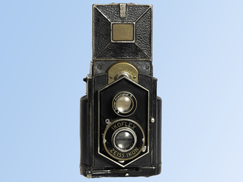 Vintage twin-lens reflex camera with weathered black body and brass fittings against blue background.