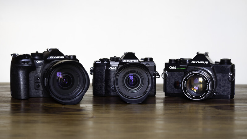 Three Olympus OM-series film cameras arranged in a row on a wooden surface.