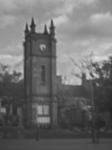 Stone church tower with clock face against dramatic cloudy sky.