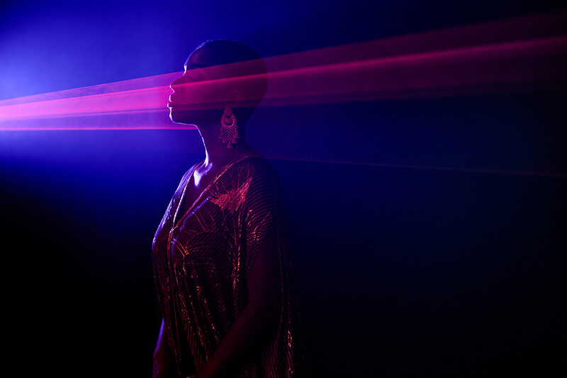 Silhouetted figure in profile with vibrant blue and magenta light rays streaming across the frame.